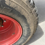 Close-up of a muddy off-road tire mounted on a bright red rim with visible lug nuts and dirt on the tread edge.