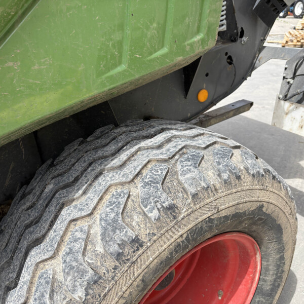 Close-up of a large off-road tire with a red rim, adjacent to a green, dirt-scratched machine body and metal framework.