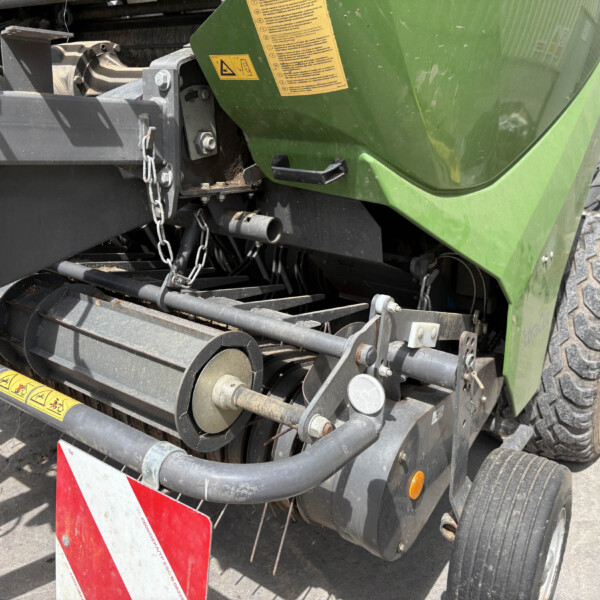 Rear view of a green harvester with belts, chains, and metal framework; warning labels and a large tire visible.