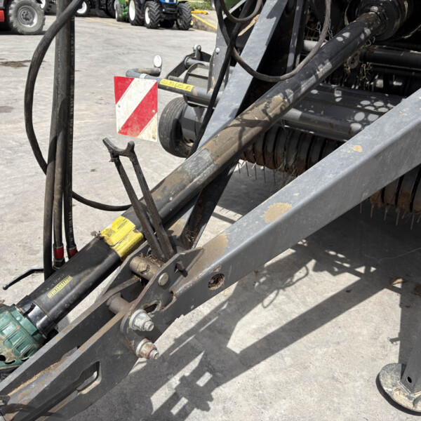 Close-up of a dusty industrial machine frame with hoses, metal beams, and a red‑and‑white safety reflector; warning stickers visible in the scene.