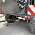 Rear view of heavy machinery on a trailer, showing large off-road tires, a red-and-white hazard plate, and exposed hydraulic components.