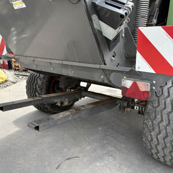 Rear view of heavy machinery on a trailer, showing large off-road tires, a red-and-white hazard plate, and exposed hydraulic components.