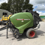 Green Fendt 4160V XtraCut baler in a yard with yellow machinery and forklift nearby.