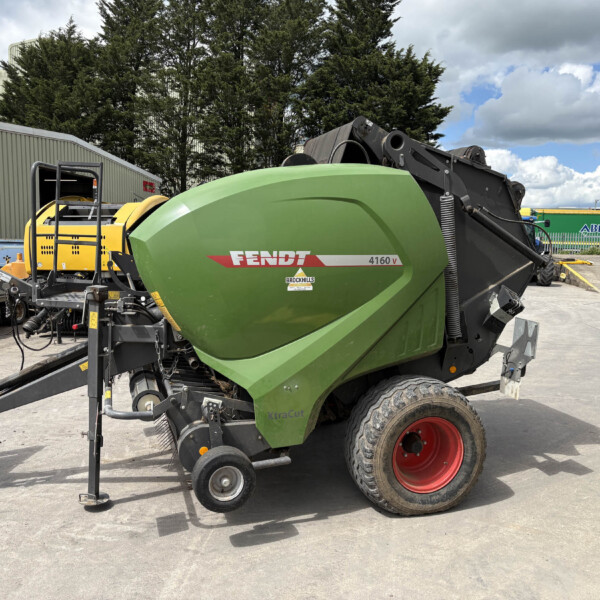 Green Fendt 4160V XtraCut baler in a yard with yellow machinery and forklift nearby.