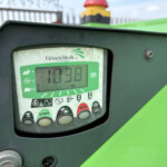 Close-up of a GreenMech control panel on a green machine, showing a green display with START and STOP buttons and warning icons.