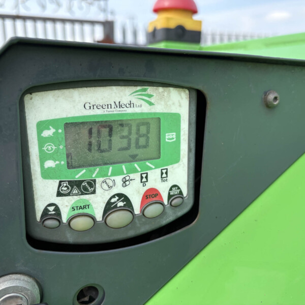 Close-up of a GreenMech control panel on a green machine, showing a green display with START and STOP buttons and warning icons.
