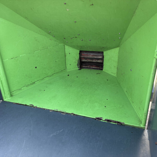 Inside a bright green dumpster with a blue floor, showing a small metal grate at the bottom center.