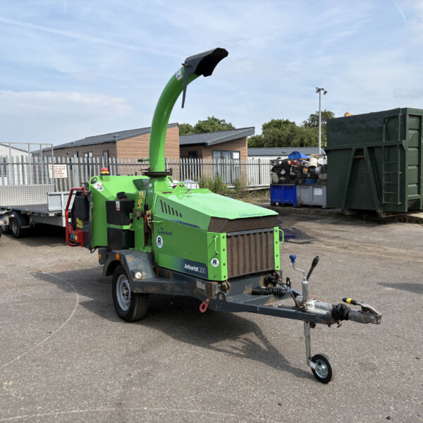 Green mobile wood chipper with tall curved chute in an industrial yard