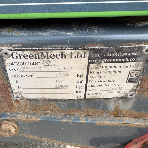 Close-up of a weathered metal plate on a GreenMech Ltd machine showing the company name and weight details, with rusty surrounding surfaces.