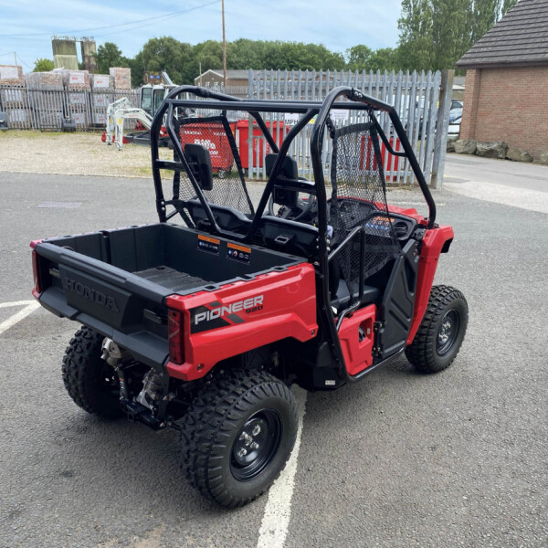 Red Honda Pioneer 520 side-by-side utility vehicle in a parking lot with a chain-link fence and industrial yard in the background