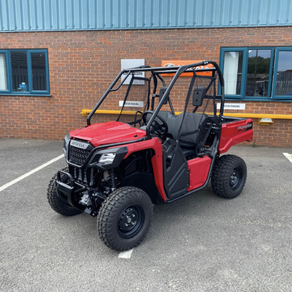Red Honda Pioneer utility vehicle parked in a marked parking space in front of a brick building with blue-framed windows.