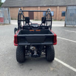 Rear view of a red Honda UTV with a cargo bed in an empty parking lot, brick building in the background.