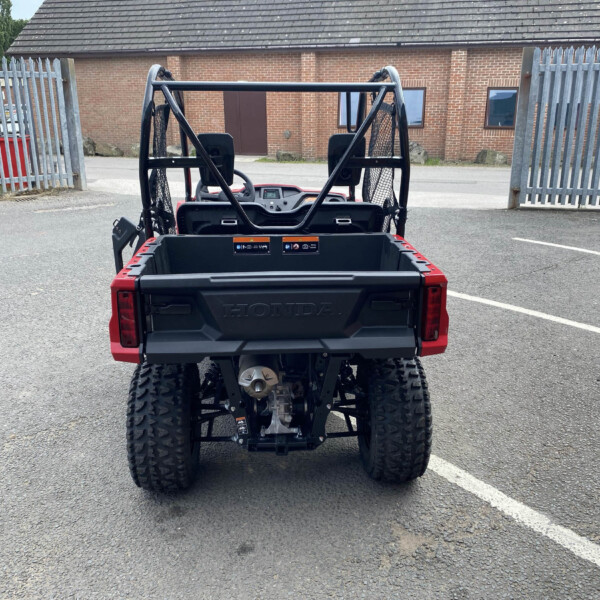 Rear view of a red Honda UTV with a cargo bed in an empty parking lot, brick building in the background.