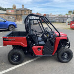 Red Pioneer S20 side-by-side utility vehicle in a parking lot, with a blue SUV and construction-yard background.