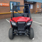 Red Honda side-by-side utility vehicle parked outside a parts shop with rugged off-road tires and roll cage.