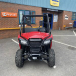 Front view of a red Honda all-terrain vehicle parked in a lot outside a parts shop.