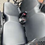 Close-up of a dark plastic vehicle seat with two red-release seat belt buckles and a mesh cargo net above the seat.