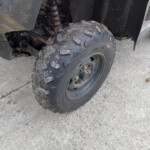 Rear tire of an off-road vehicle with muddy, chunky tread and visible suspension components behind it