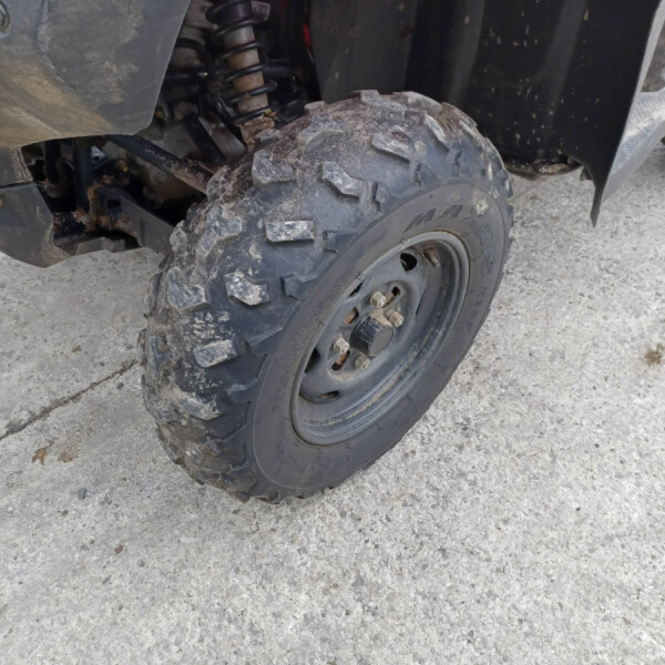 Rear tire of an off-road vehicle with muddy, chunky tread and visible suspension components behind it