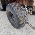Close-up of a muddy off-road tire on a quad bike, showing deep tread and dirty wheel hub.