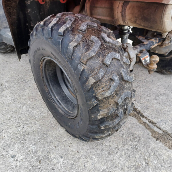 Close-up of a muddy off-road tire on a quad bike, showing deep tread and dirty wheel hub.