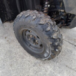 Front wheel of an off-road vehicle with muddy tire and visible suspension components behind it