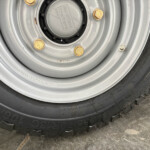 Close-up of a car wheel: gray steel rim with brass lug nuts and a center cap, surrounding a black tire bead.