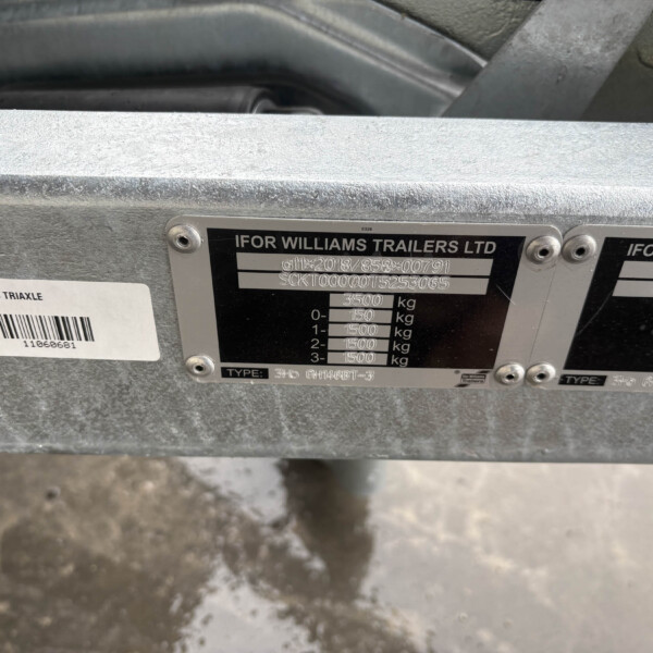Close-up of a metal trailer identification plate on an Ifor Williams trailer, showing the brand name, weight data, and a nearby barcode sticker.