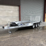Metal loading trailer parked in a wet industrial yard with a large corrugated metal door and yellow access door in the background.