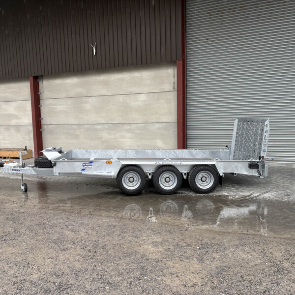 Flatbed trailer parked in front of a brown corrugated-metal wall and large gray roll-up door at an industrial site.