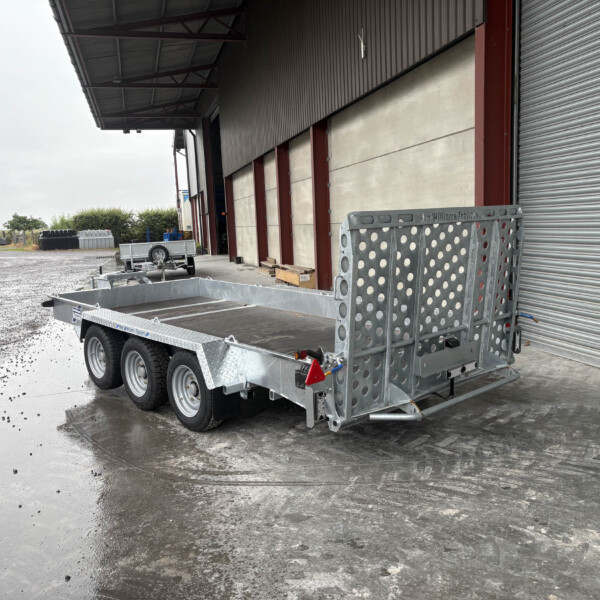 Industrial loading area with a large corrugated metal building, roller shutter door, and a wheeled trailer in the foreground on a wet concrete surface.
