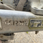 Close-up of a dusty metal trailer hitch with embossed license-style numbers and a worn label plate nearby.