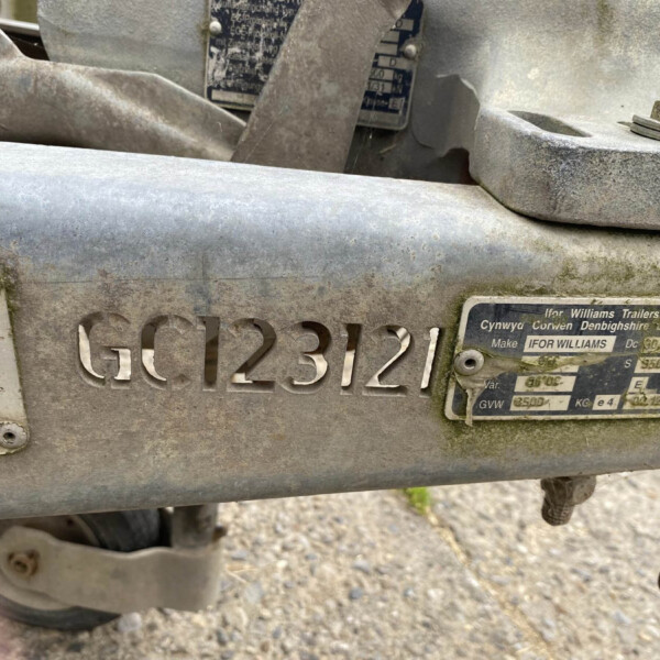 Close-up of a dusty metal trailer hitch with embossed license-style numbers and a worn label plate nearby.