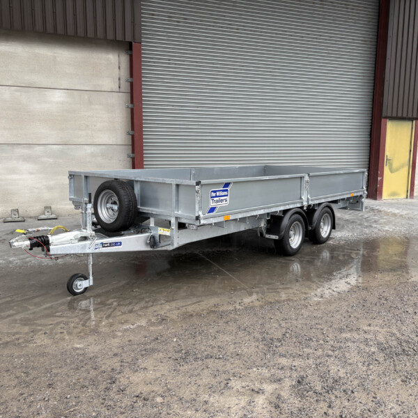 Metal-framed trailer parked in front of a large corrugated shutter and yellow door in an industrial building, wet ground with puddles nearby.