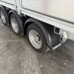 Close-up of a metal trailer undercarriage with triple wheels and tires on a concrete floor.