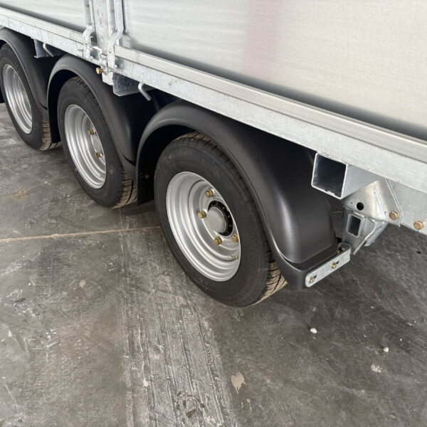 Close-up of a metal trailer undercarriage with triple wheels and tires on a concrete floor.