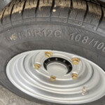 Close-up of a car tire and steel wheel, showing tread pattern and lug nuts. The tire sidewall displays size markings (195/60R12C).