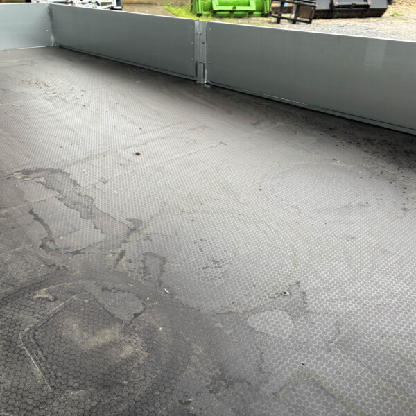Open cargo bed of a metal trailer with gray sidewalls and a textured anti-slip floor.