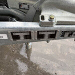 Close-up of a trailer chassis showing weight-label plates and a bolt on a gray metal beam, with concrete floor below