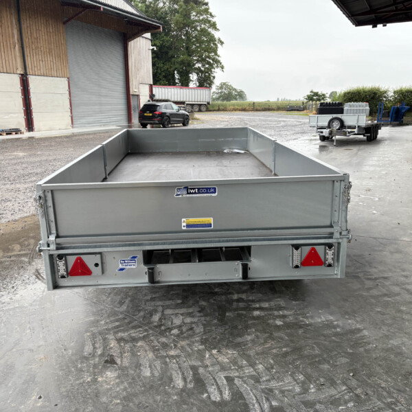 Large gray open-top trailer viewed from behind in an industrial yard with a car and a truck trailer in the background.