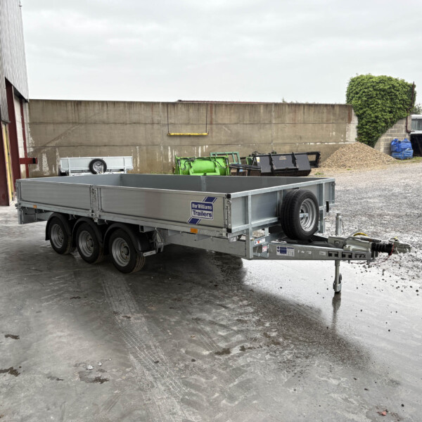 Flatbed trailer with spare tire parked outside a warehouse, beside a gray corrugated door and concrete wall.