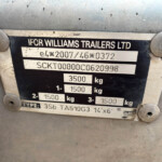 Close-up of a trailer identification plate mounted on a dirty metal surface, showing the company name and weight specifications