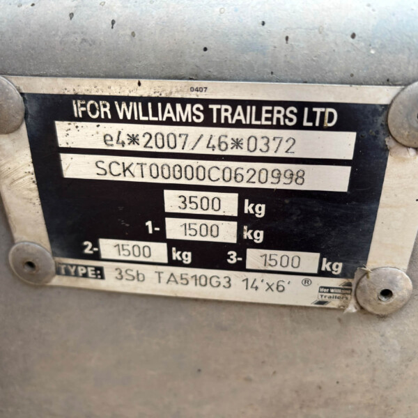 Close-up of a trailer identification plate mounted on a dirty metal surface, showing the company name and weight specifications