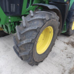 Green tractor with large muddy rear tires and yellow rims viewed from the side on a concrete surface