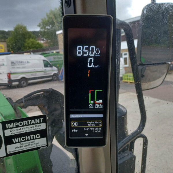 Close-up of a tractor cab digital display showing 850 n/min RPM and 0 km/h, with workshop yard visible outside the window.