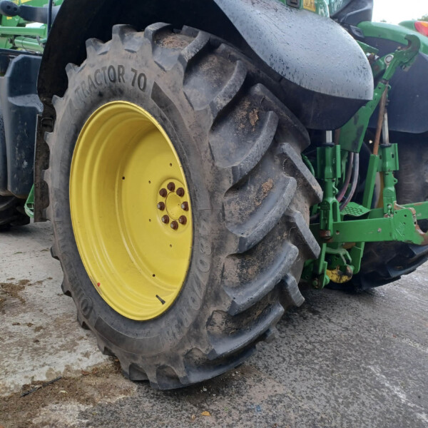 Close-up of a large tractor rear wheel with a bright yellow rim and chunky muddy tread, part of a green agricultural machine in a yard.