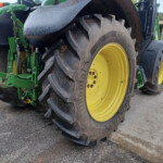 Close-up of a green tractor with large yellow-rimmed rear tires outdoors, showing muddy treads and machinery frame to the left.