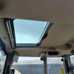 Inside a vehicle cabin looking up at the open sunroof with blue sky visible; raindrops on the windows and dashboard nearby.
