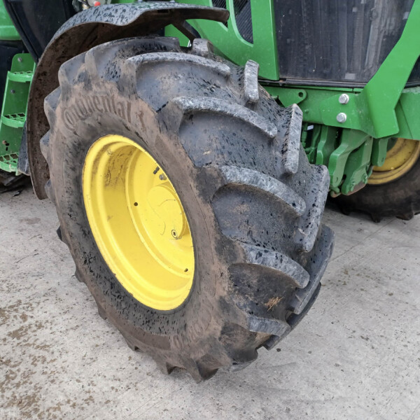Close-up of a muddy tractor tire with a yellow rim and green body nearby on a concrete floor
