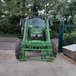 Front view of a green John Deere tractor with loader arms, large tires, and orange beacon lights on top, parked outdoors.